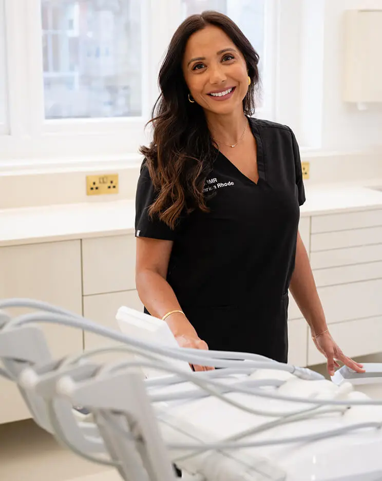 Dr Manrina Rhode, cosmetic dentist, beside a dental chair at DRMR Clinic in Knightsbridge, London